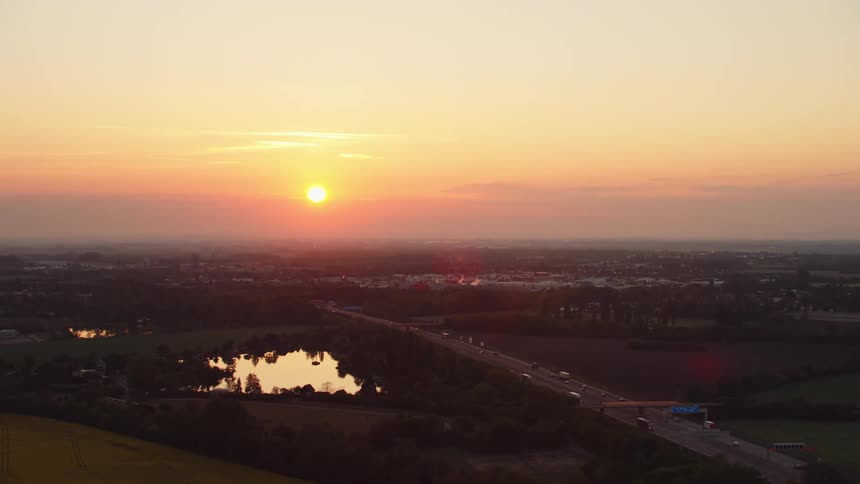 Sun sinks toward the horizon turning fog and sky orange over town highway leads toward