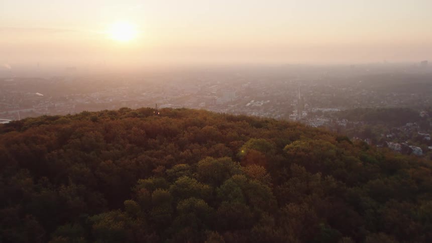 Sun shines through heavy fog covering town nestled among trees near heavily forested mountain