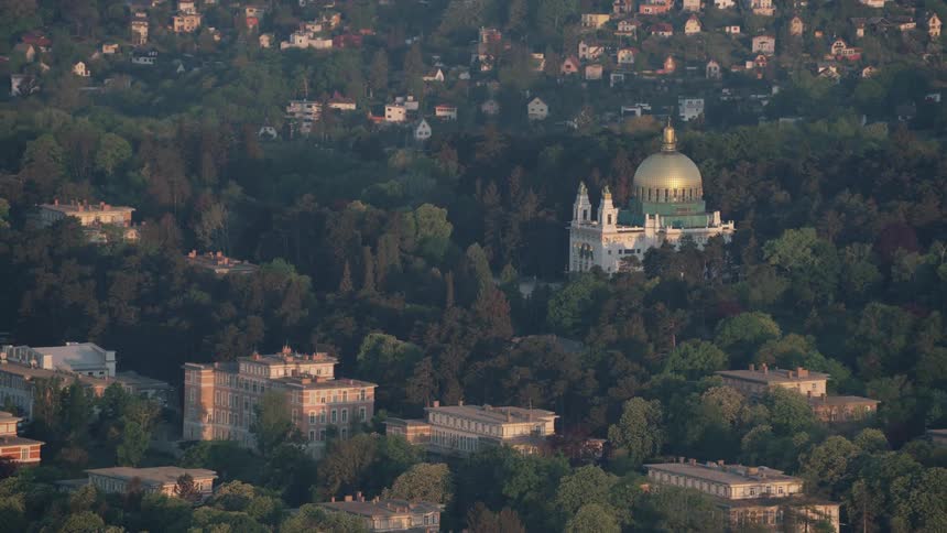 Green trees surround the gold dome of a church building and the buildings and homes in the surrounding hills
