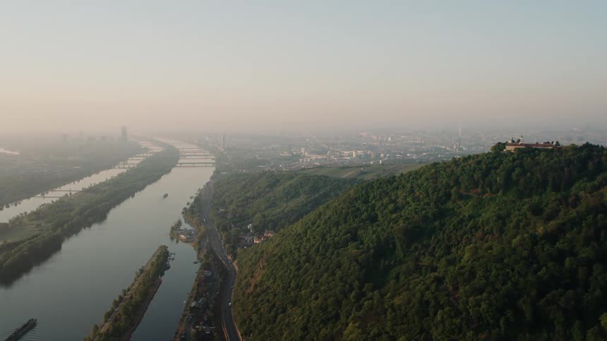 An aerial view of hills covered with trees is displayed by a river