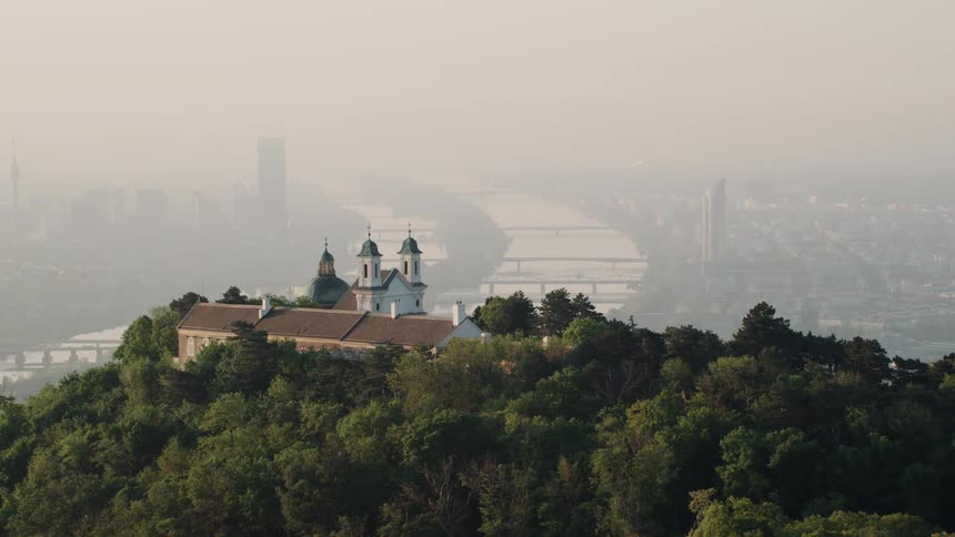 A building a forest on a tall hill overlooking a city shrouded in fog