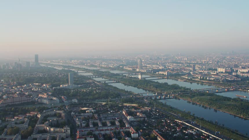 The smooth river surface reflects sky and trees as it cuts through a large city