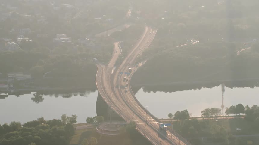 Cars and trucks on a highway cross over a river that is reflecting the sky and surrounding trees