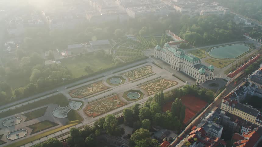 A palace with ornately manicured gardens and grounds surrounded by city buildings
