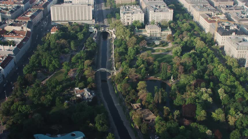 River surrounded by forested park flows past buildings parallel to streets