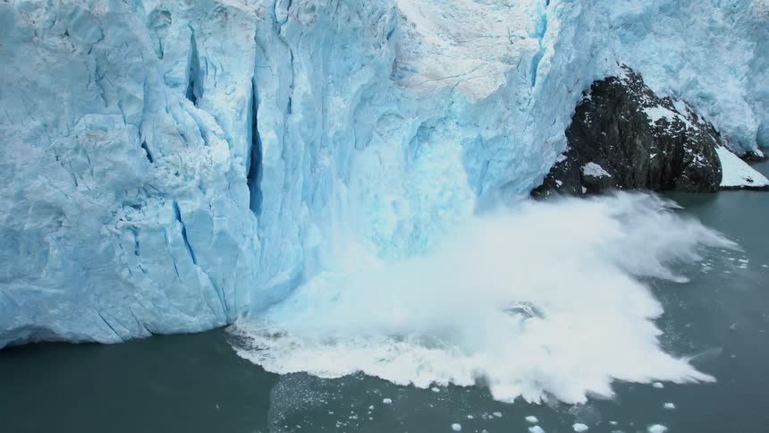 A large chunk of snow falls off a cliff and in to the water