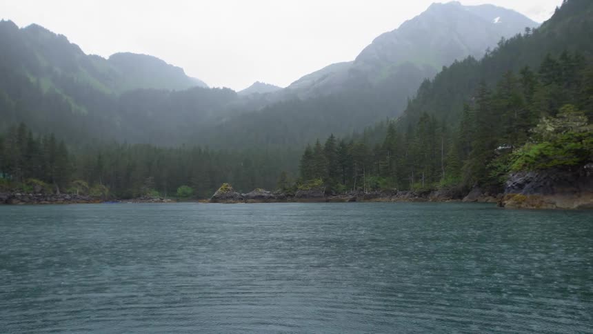 Rain falls on a lake in the mountains surrounded by pine tree forest