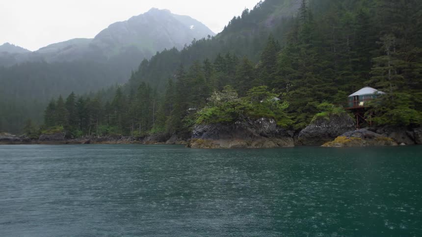 A house near a lake with trees and mountains in the background