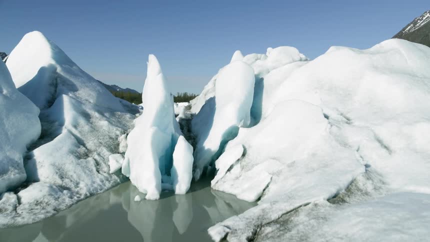 Small icebergs and ice float on water reflecting the sky and surrounding mountains