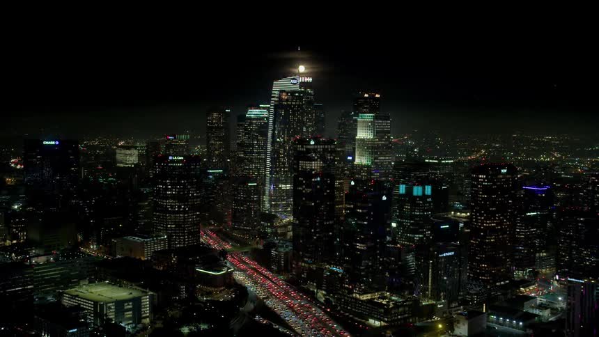 A city skyline at night with buildings and skyscrapers with the moon in the background