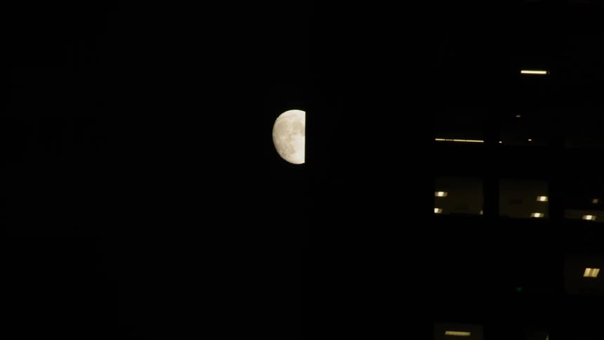 Full moon at night passing behind city buildings