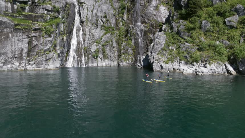 Three people paddle board towards a water fall