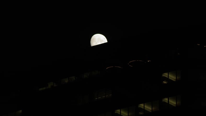 Large moon is slowly lost behind building at night