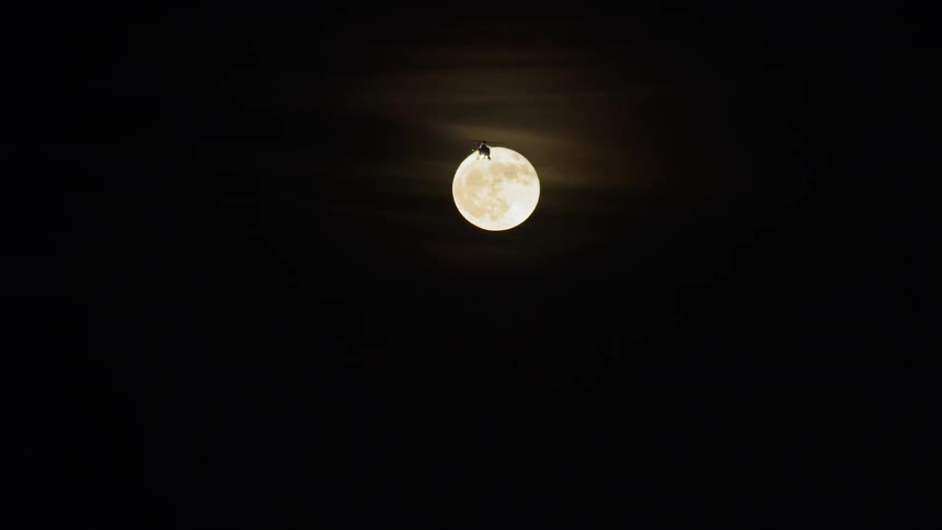 A helicopter flying in front of the full moon during the night
