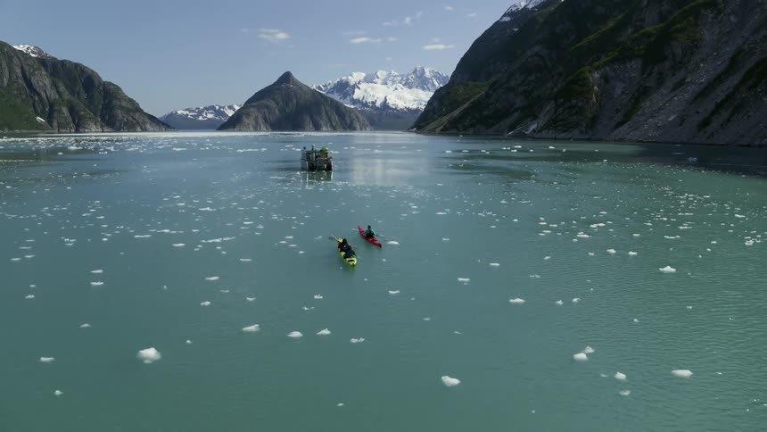 Kayakers paddle through blue tinted water dotted with floating ice
