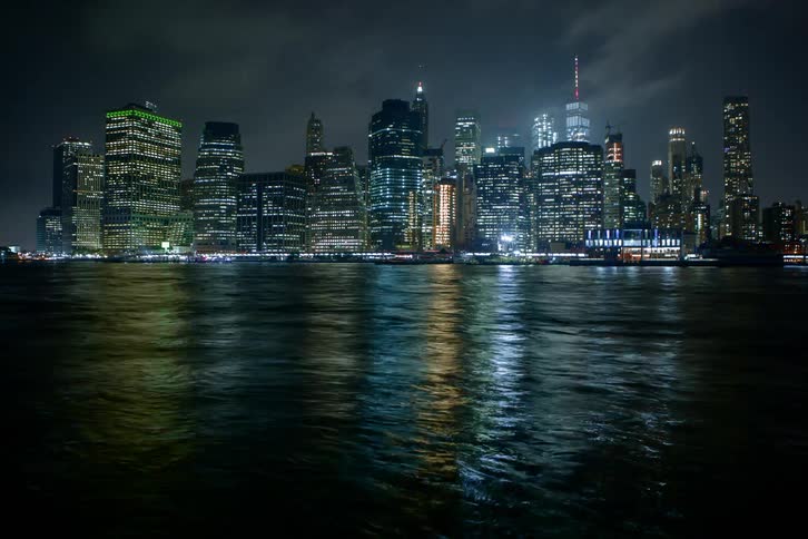 Lights from the city skyline and passing boats shimmer and shine on the surface of the water at night