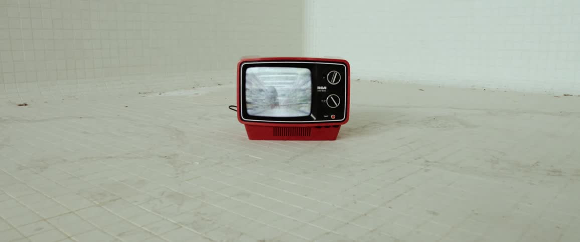 A small tv is sitting in an empty pool playing images of a woman in a grocery store