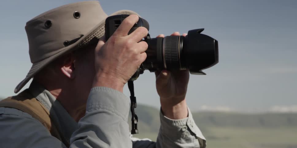 A man in a hat takes pictures outside