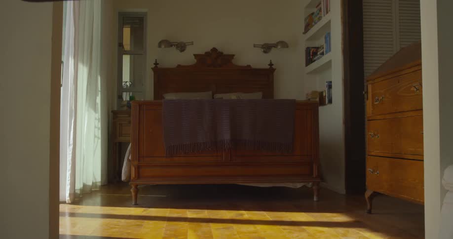 A empty bedroom has curtains blowing on the side