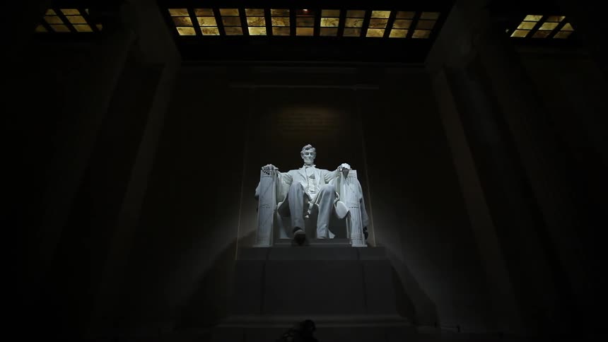 A person walks in front of the lincoln memorial and picks up their coat
