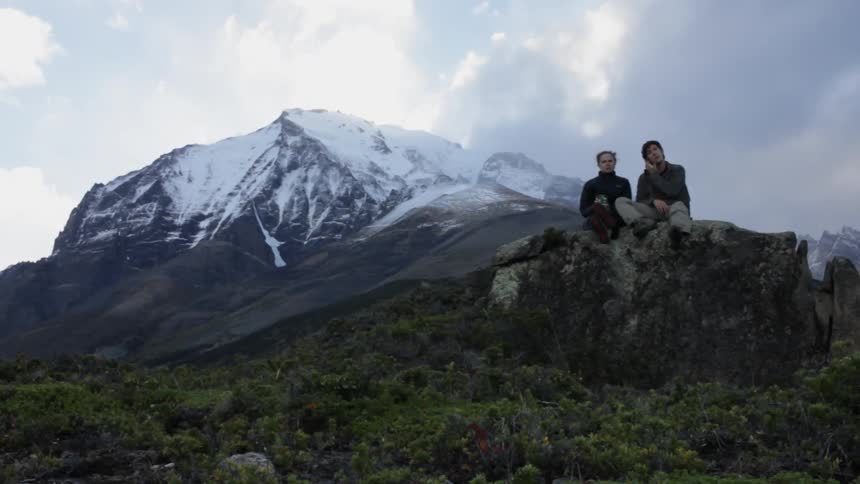 Two people sit on a mountain rock and talking