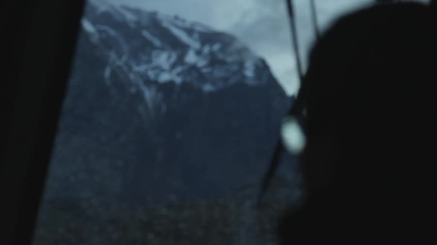 A man is looking out the window towards a snow covered mountain