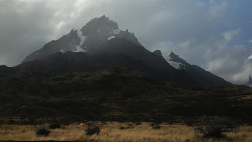 A large mountain covered in snow is beyond this yellow field