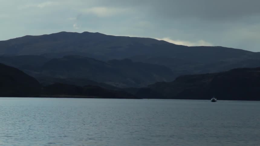 A body of water at the base of a mountain on a cloudy day