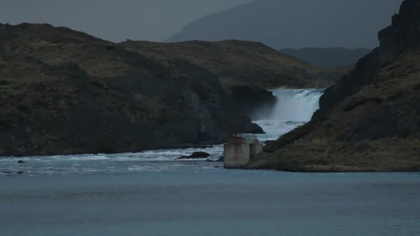 A waterfall gushes towards an open body of water