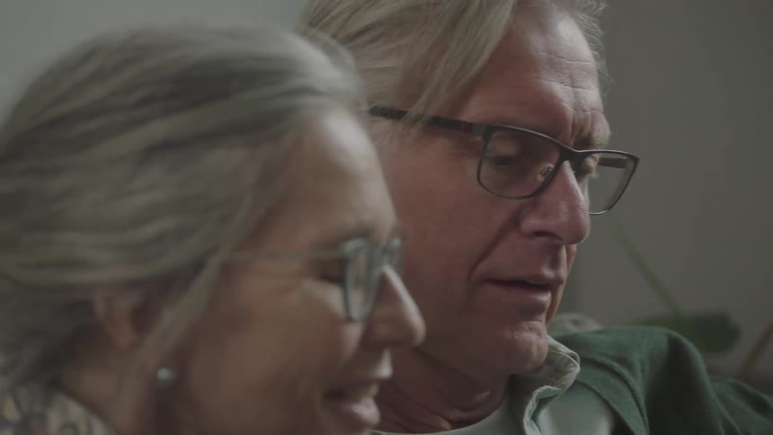 Elderly man and woman sitting on the sofa use a smartphone together in the living room