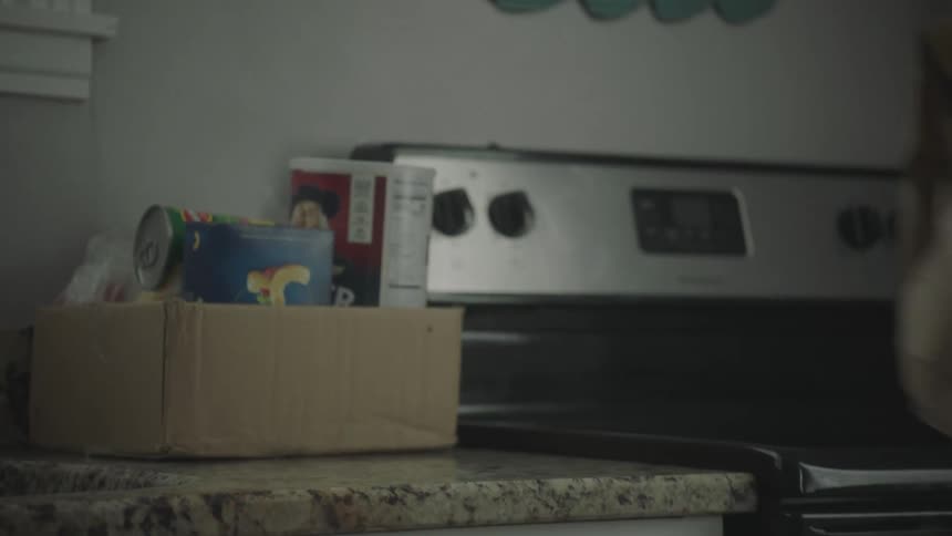 Box of food and paper bag with yellow heart being placed on kitchen counter
