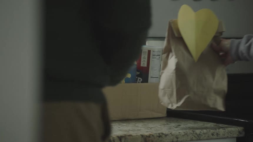A man and woman put groceries and a paper bag with a heart on a counter
