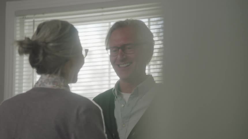 An older couple dances happily in their home