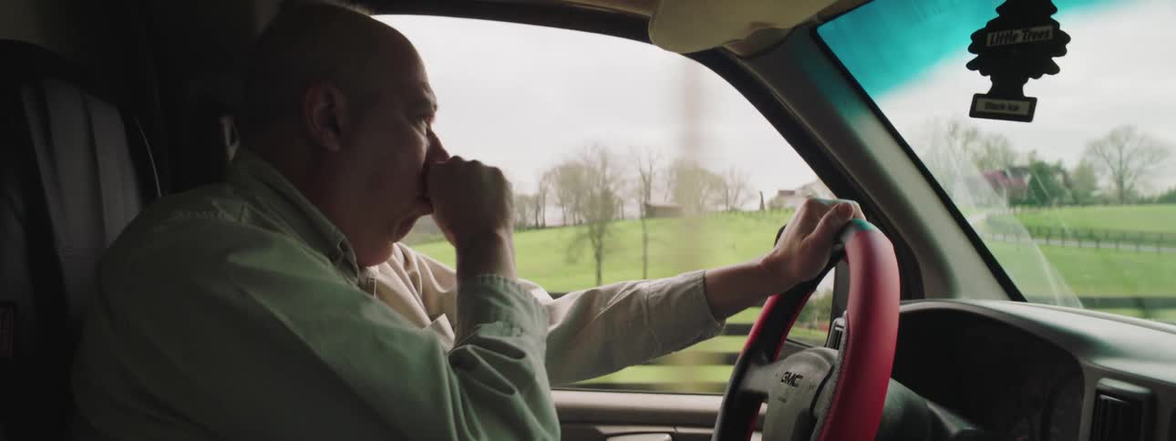Man coughs on his hand and out the window while driving car