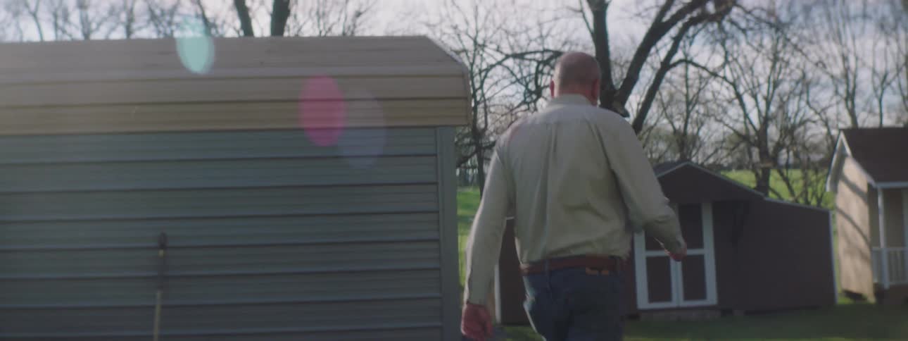 Man walks across yard to garage and raises garage door