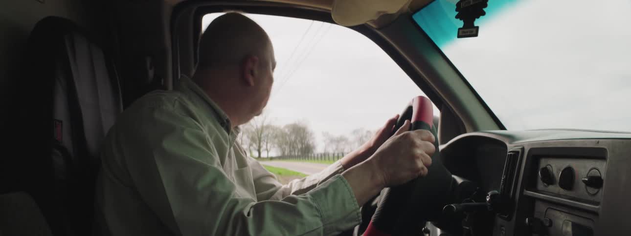 A man driving a truck past homes and farm fields