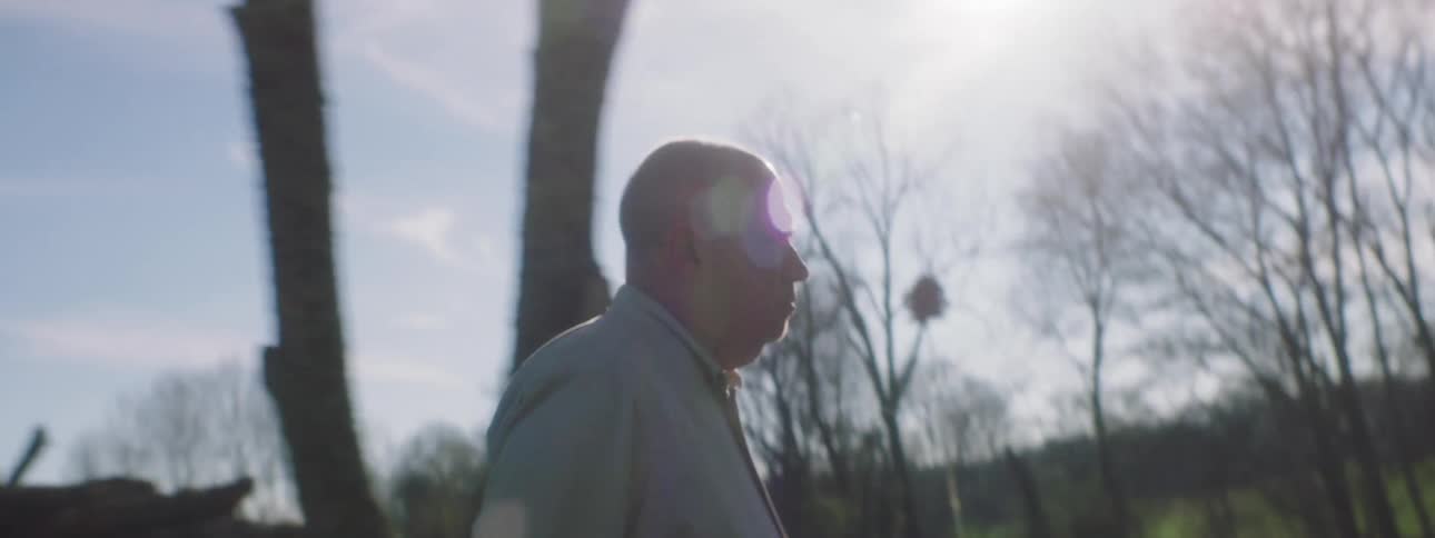 A man raises his hand and coughs into it while walking to a large detached shed