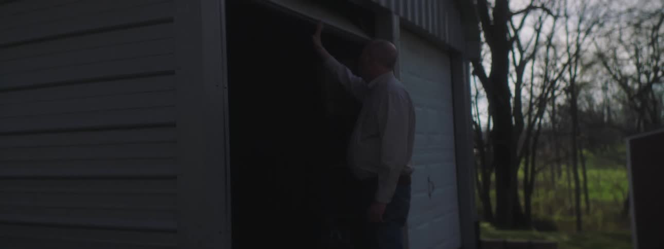 An older man coughs as he walks to and opens his garage door