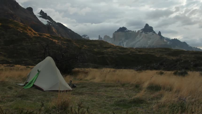 A small tent sits on a field before a mountain range