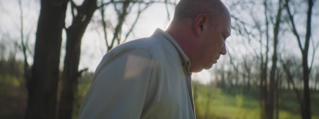 A middle aged man coughing while standing in a woodland