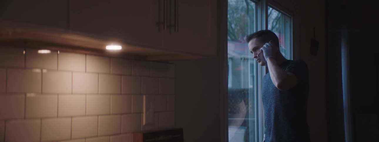 Male speaking on cellphone while standing and looking out a sliding glass door