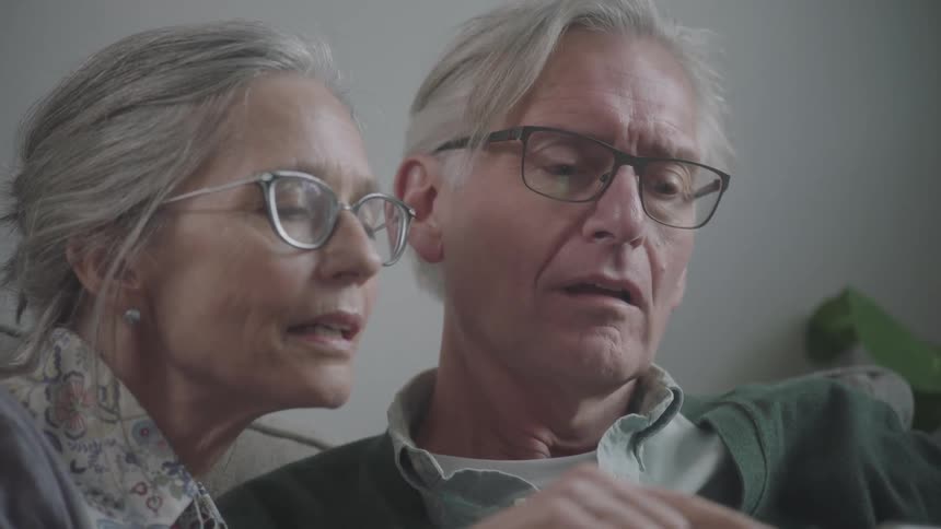 Elderly couple check smartphone while sitting in couch