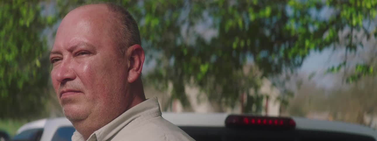 A man coughing while standing outdoors next to a pickup truck