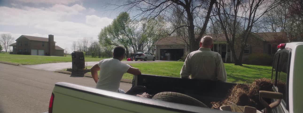 A pair of men relaxing against a truck parked in front of a house