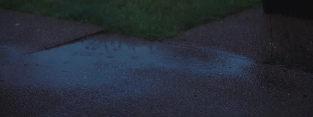 Rain drops forming a small puddle on sidewalk near the grass