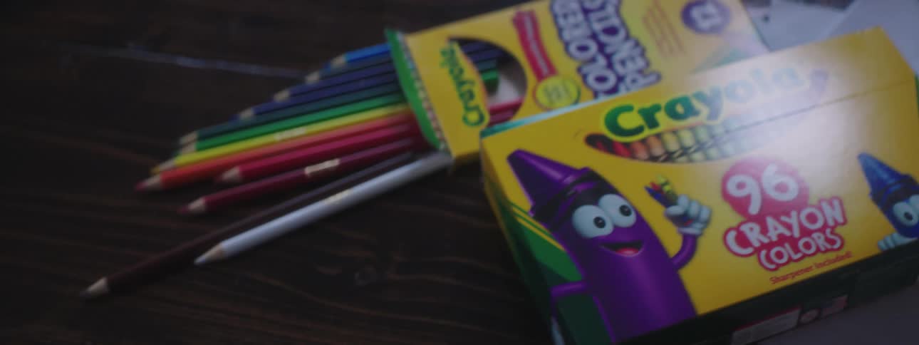 A person quickly removes the flower center piece off the wooden dining table and crayons and colored pencil are tossed onto the table