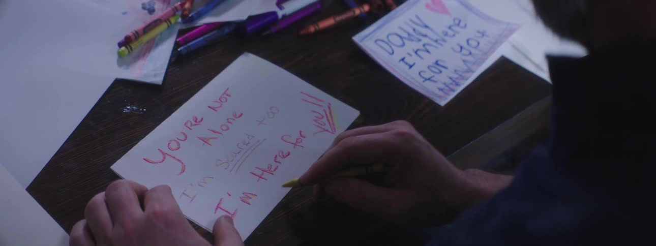 Man sitting at table writes signs on paper with crayons