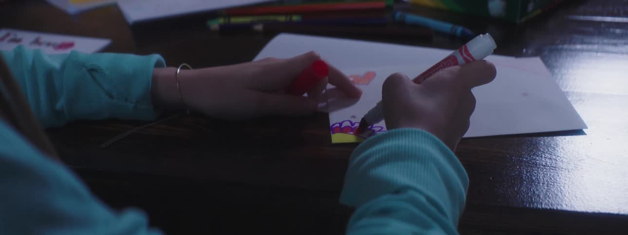 A girl uses a marker to color a card at the dining room table