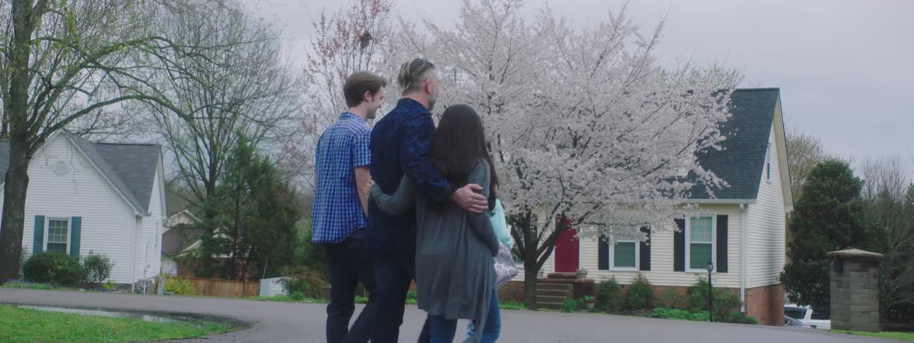 A man and woman walk with their arms around each other with their two children on a road in the neighborhood