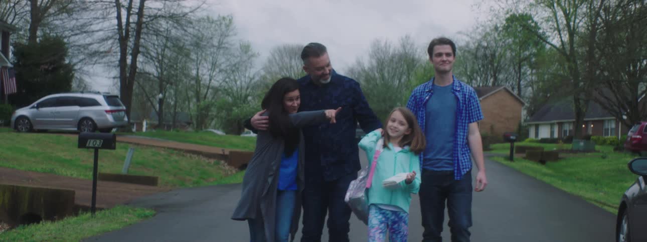 A family walks down a neighborhood street and a little girl puts notes on cars